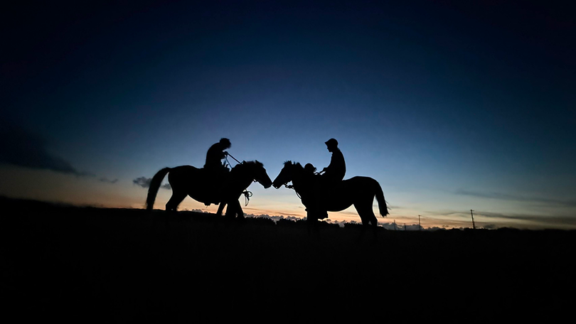 Two people are riding horses at night.